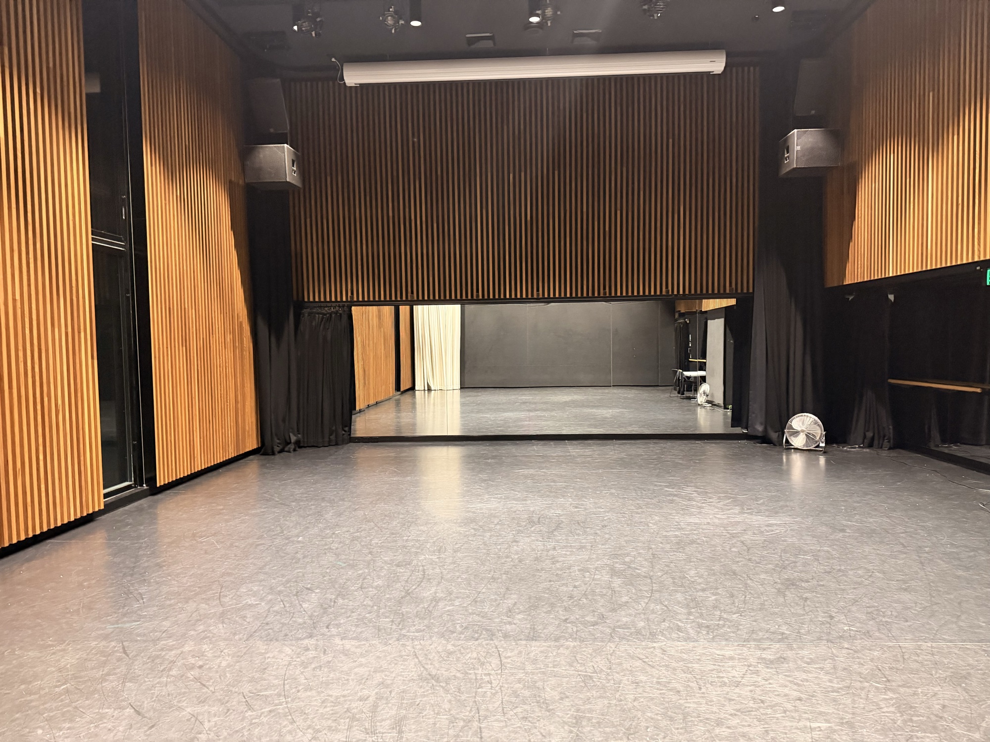 A large empty rehearsal room with a mirrored wall, wood-panelled walls and a grey sprung floor