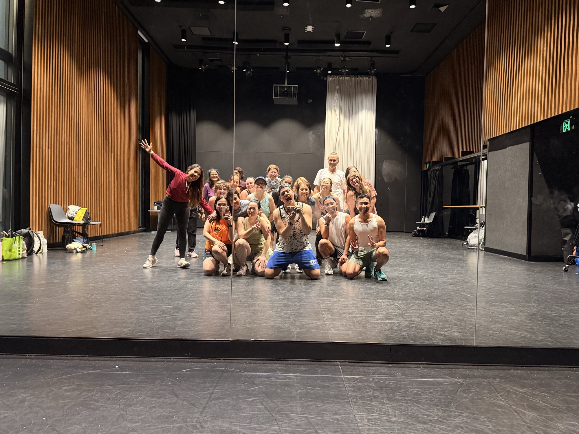 A whole Zumba class strikes a playful group pose together in a large, mirrored wood-panelled room