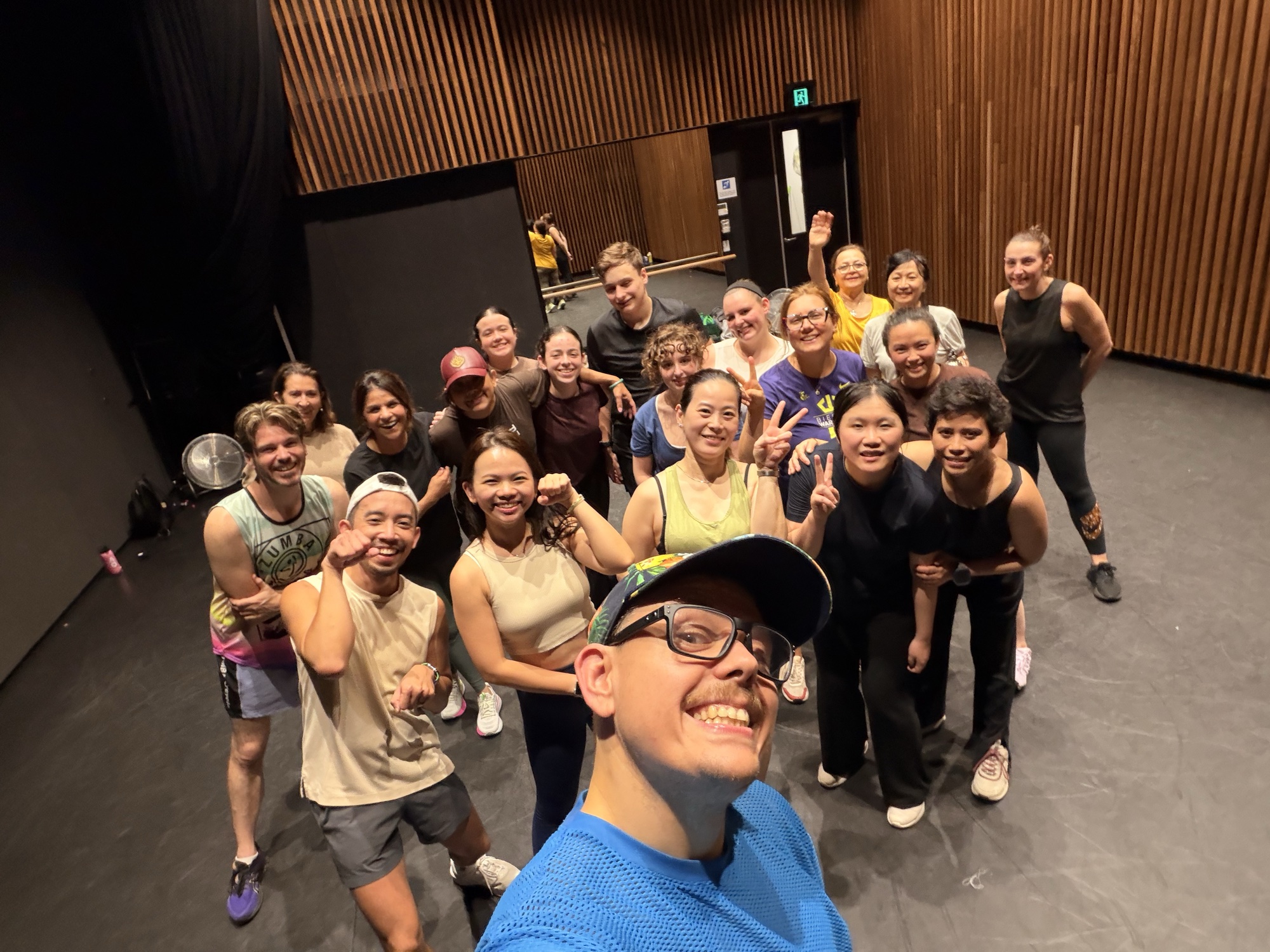Pawel grins close to the camera, arm out for a selfie, with a big group of dancers smiling behind him