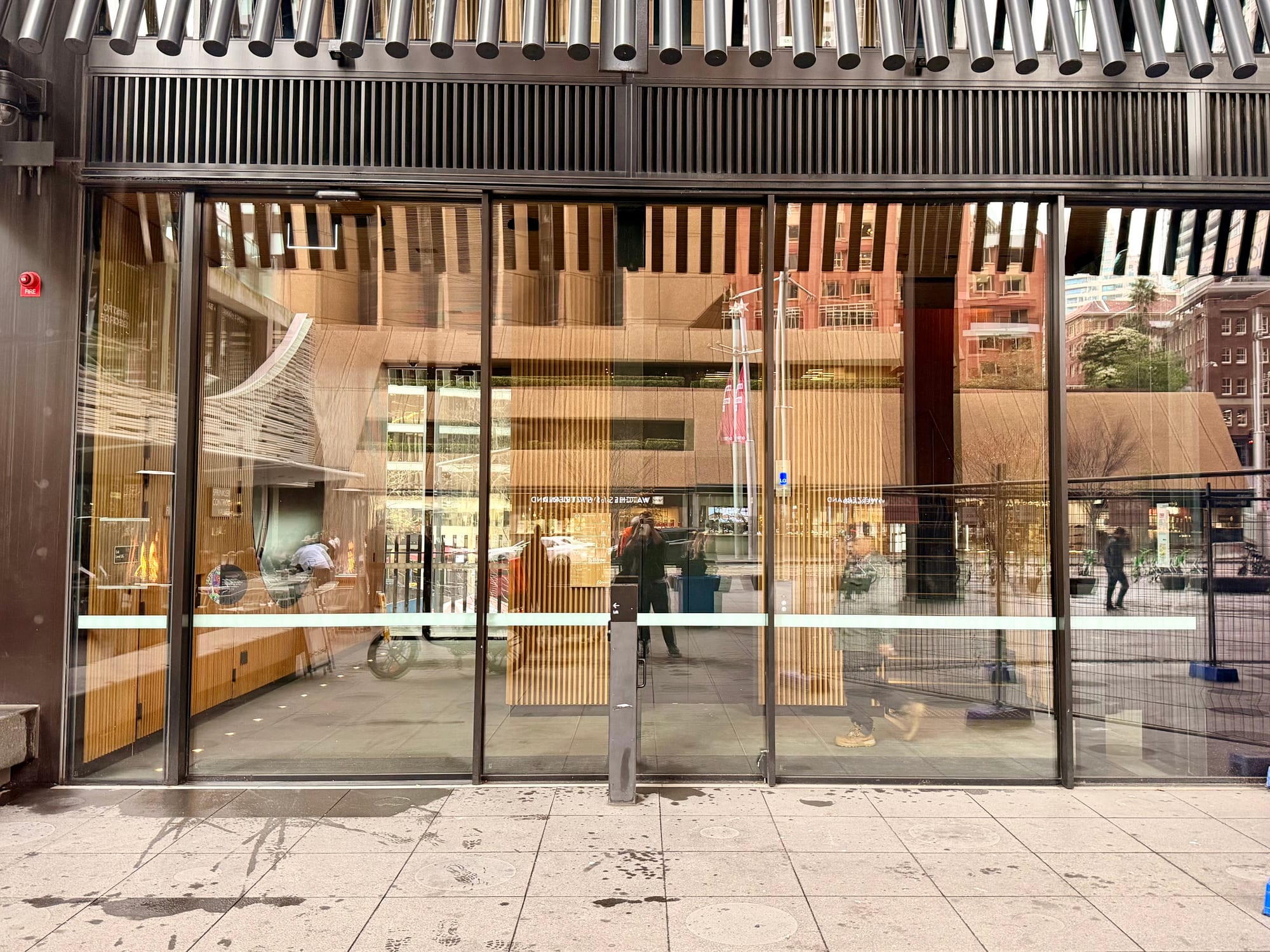 A glass street-level frontage with warm wood-panelled walls visible inside, on a city footpath