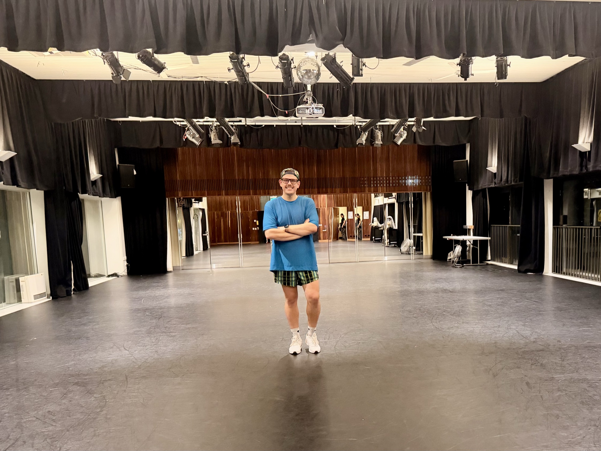 Pawel stands with his arms crossed, smiling, in a large hall with a mirrored wall and a disco ball overhead